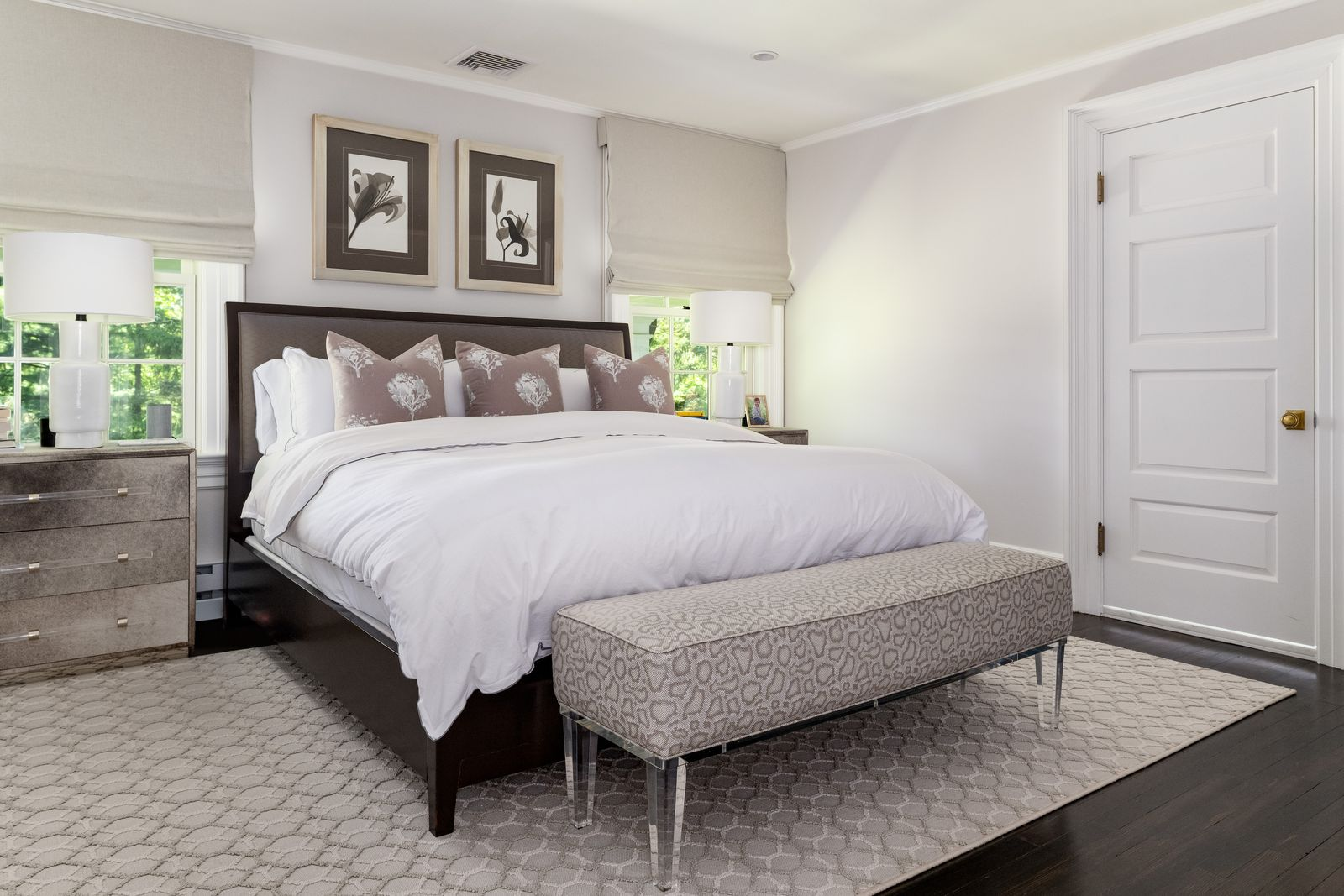 The bedroom itself is designed in a soft neutral palette, with dark hardwood floors and windows on either side of the bed.