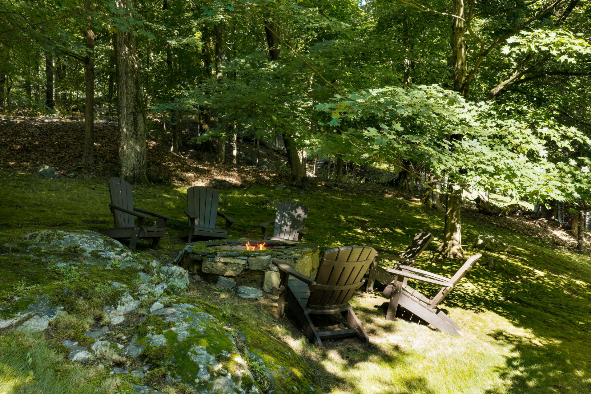 Tucked farther up a hill, a secluded stone fire pit surrounded by Adirondack chairs sits within a rocky, tree-covered section of the grounds.