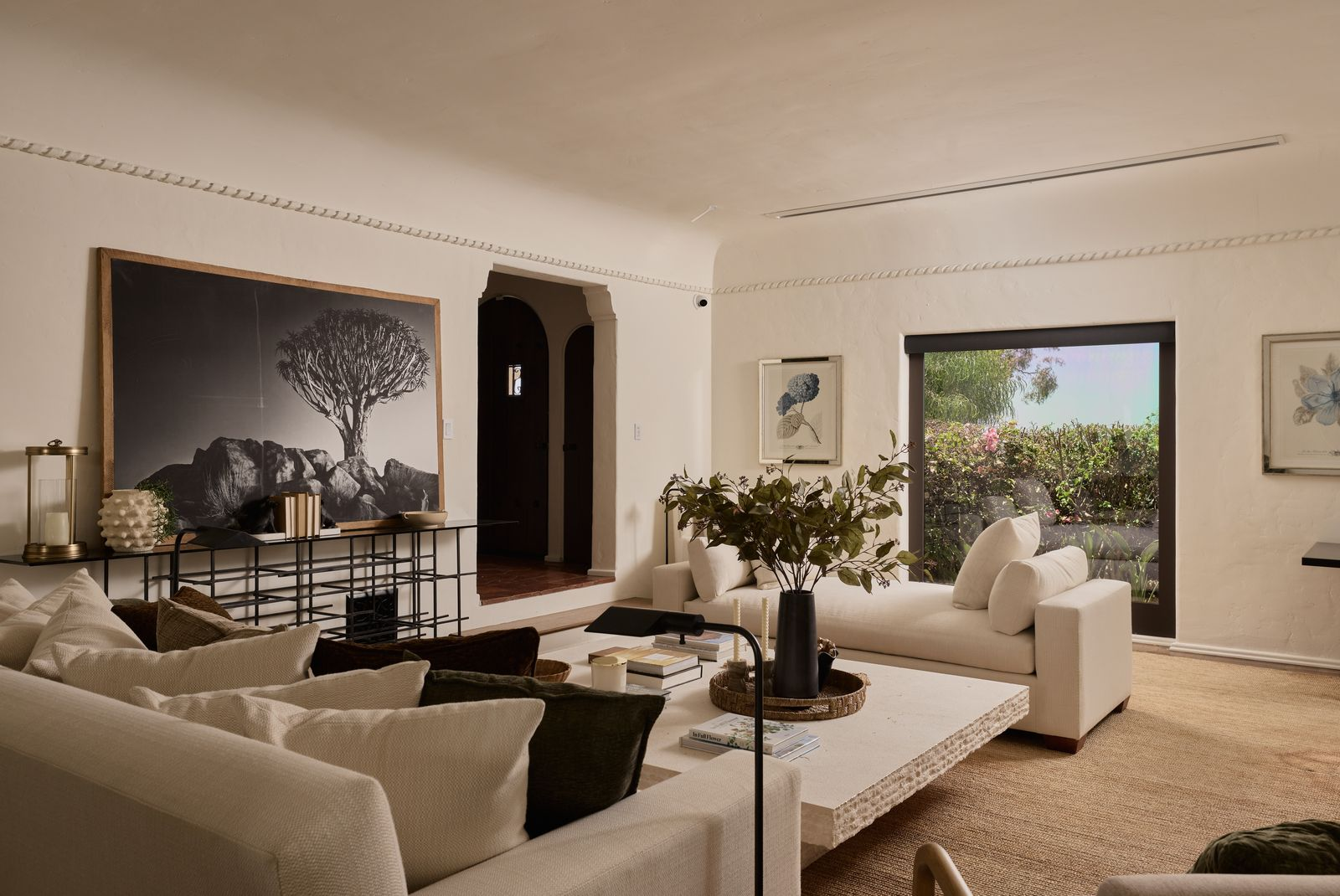 Cream-colored plaster walls, dark wood floors, and rope-like molding near the ceiling give the room a Mediterranean look, while a picture window bring color into the room.
