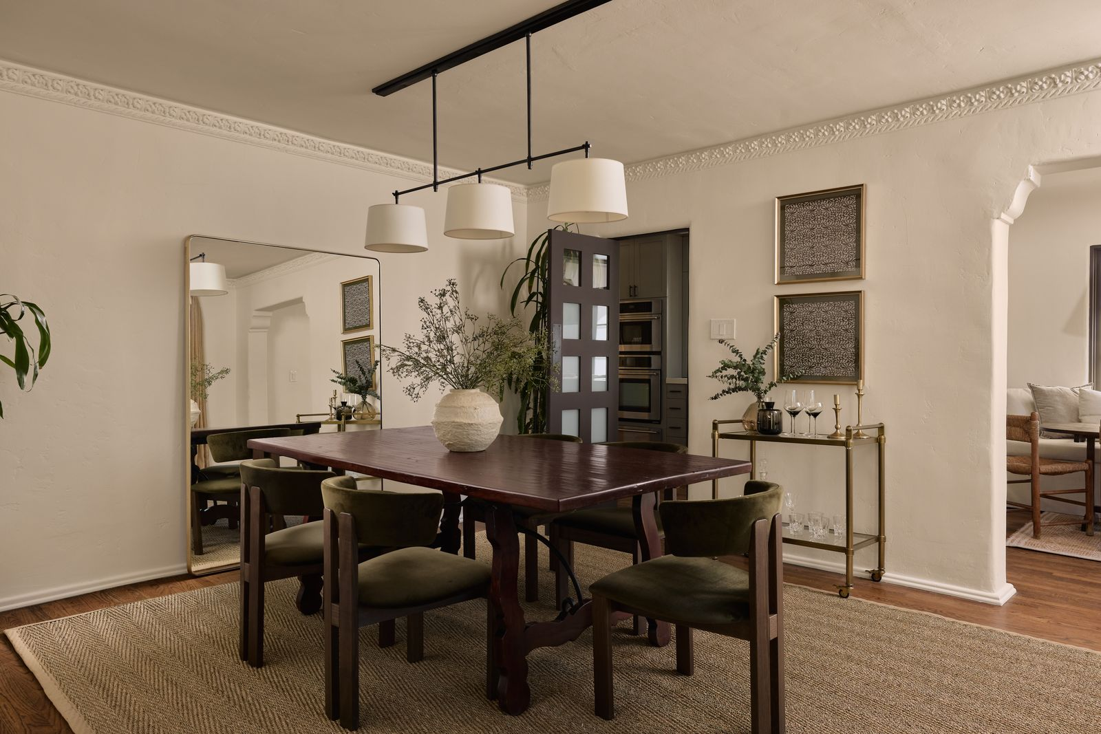 The formal dining room has a long rectangular table surrounded by six olive green velvet chairs in the center of the room. 