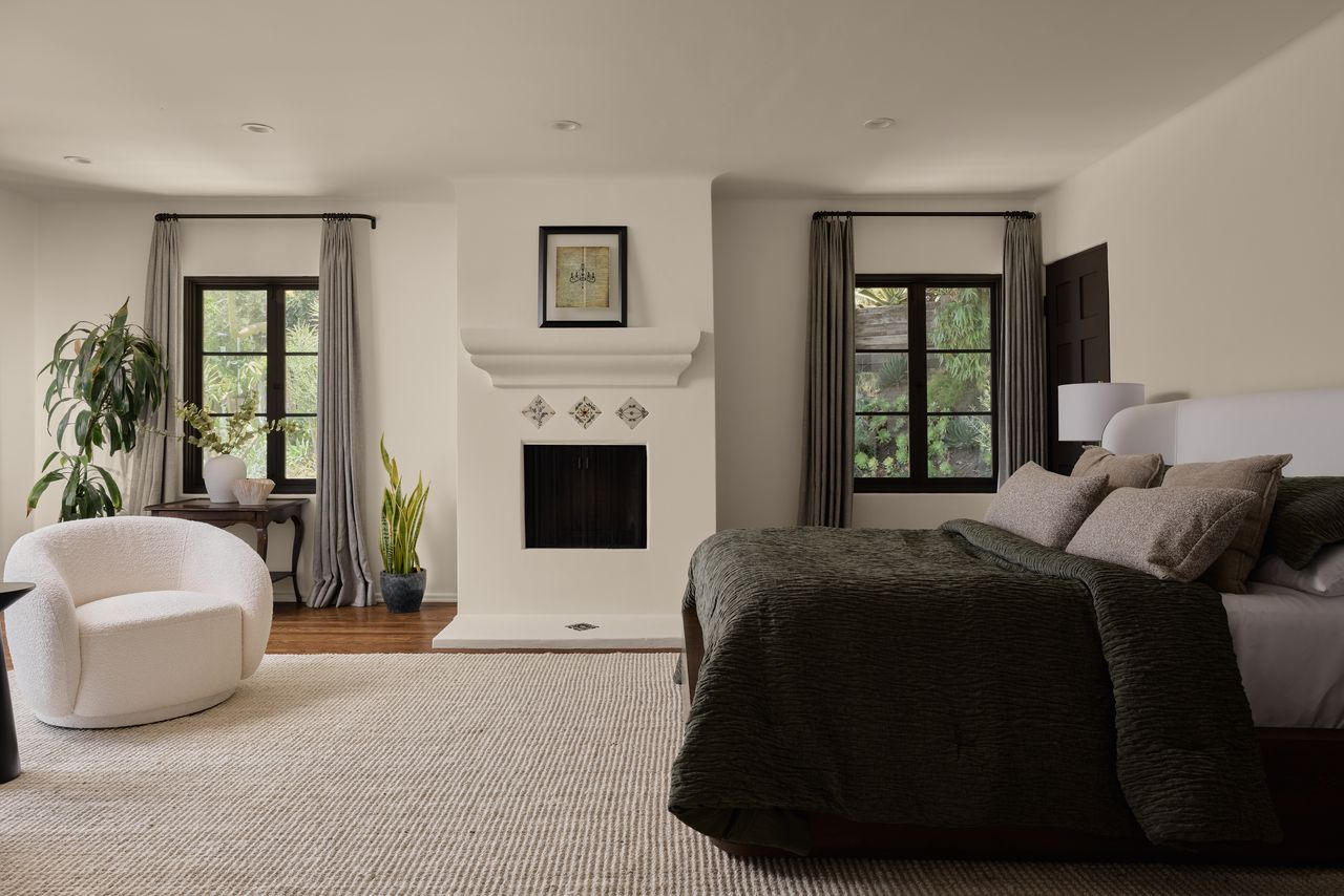 Upstairs, the primary bedroom has a fireplace with a sculpted plaster surround in the middle of two windows.
