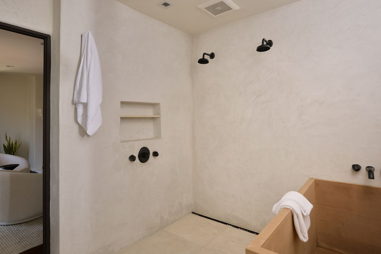 On the other side, a deep soaking tub sits inside an open shower with wall-mounted fixtures and dual showerheads.