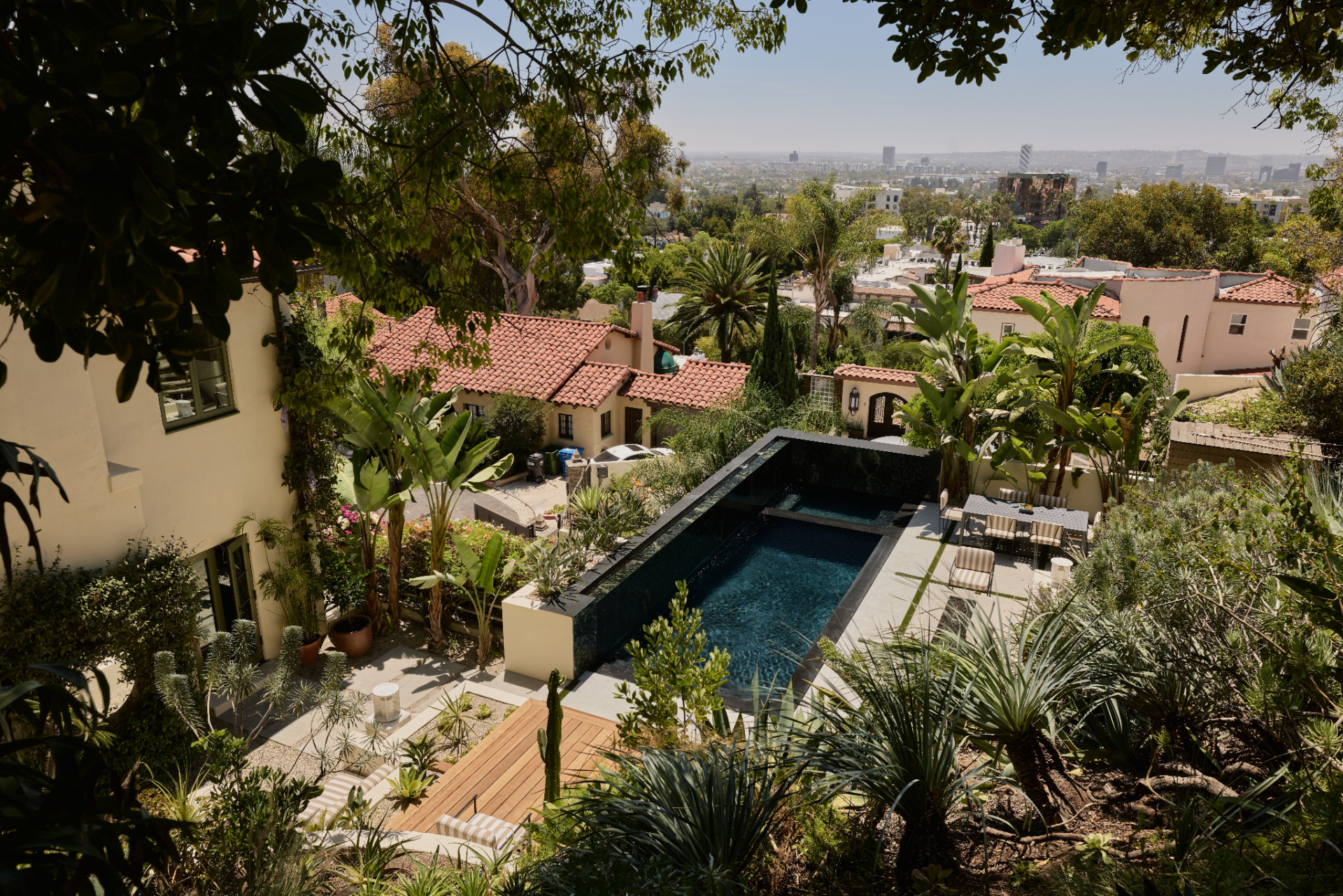The dark-bottom pool and spa runs alongside these spaces, framed by pale paving and a wall of cascading water. 