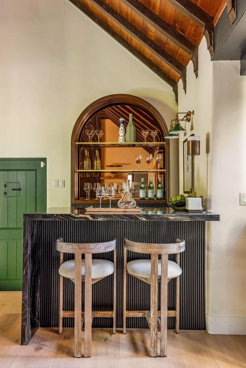 The bar pairs a black fluted base and dark stone counter with brass-trimmed open shelving that rises above the bar to display glassware and bottles.