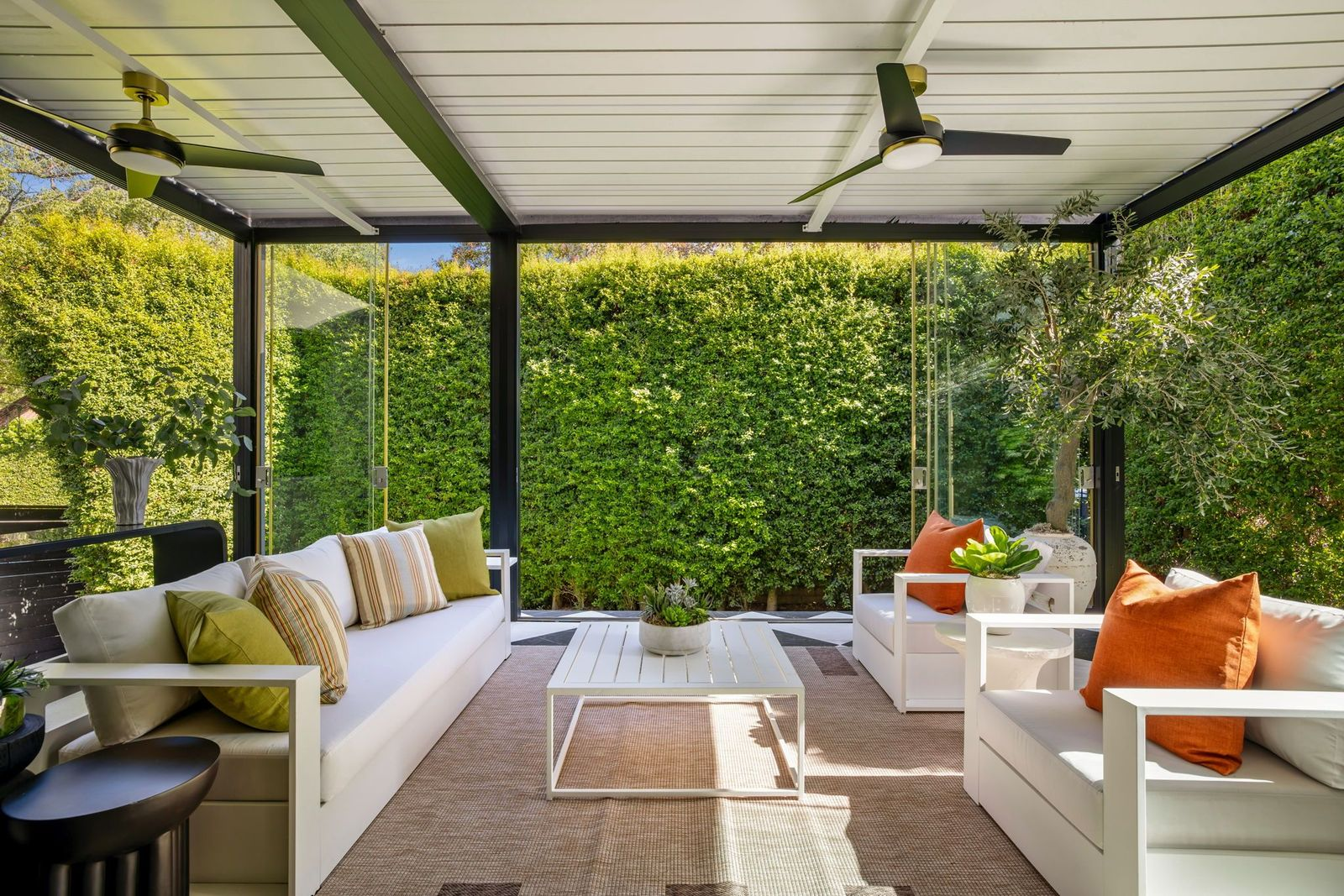 The sunroom where glass walls surround white sofas and armchairs gathered around a low central table.