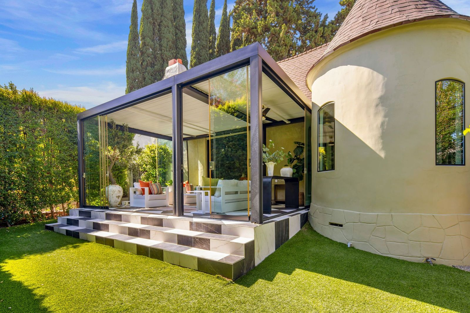 Large sliding doors can be pulled open along multiple sides, connecting the room directly with the backyard just past a short set of black-and-white marble steps.