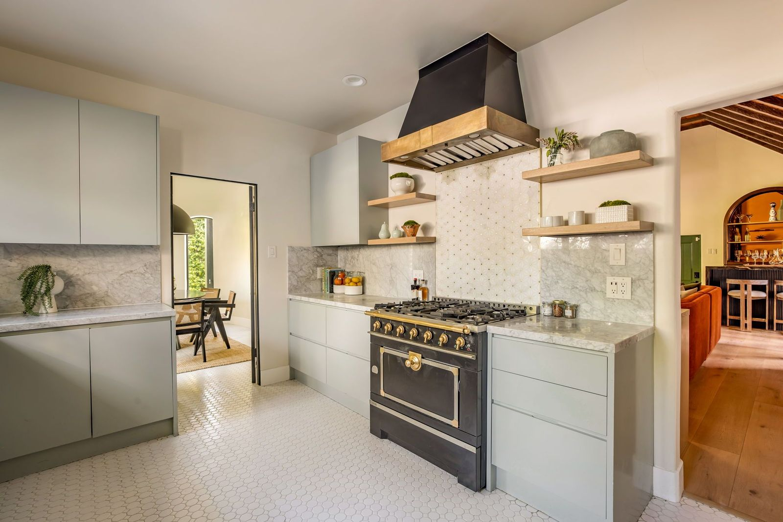A black-and-brass range beneath a matching hood, with open wood shelving and patterned tile adding detail around the cooking area.