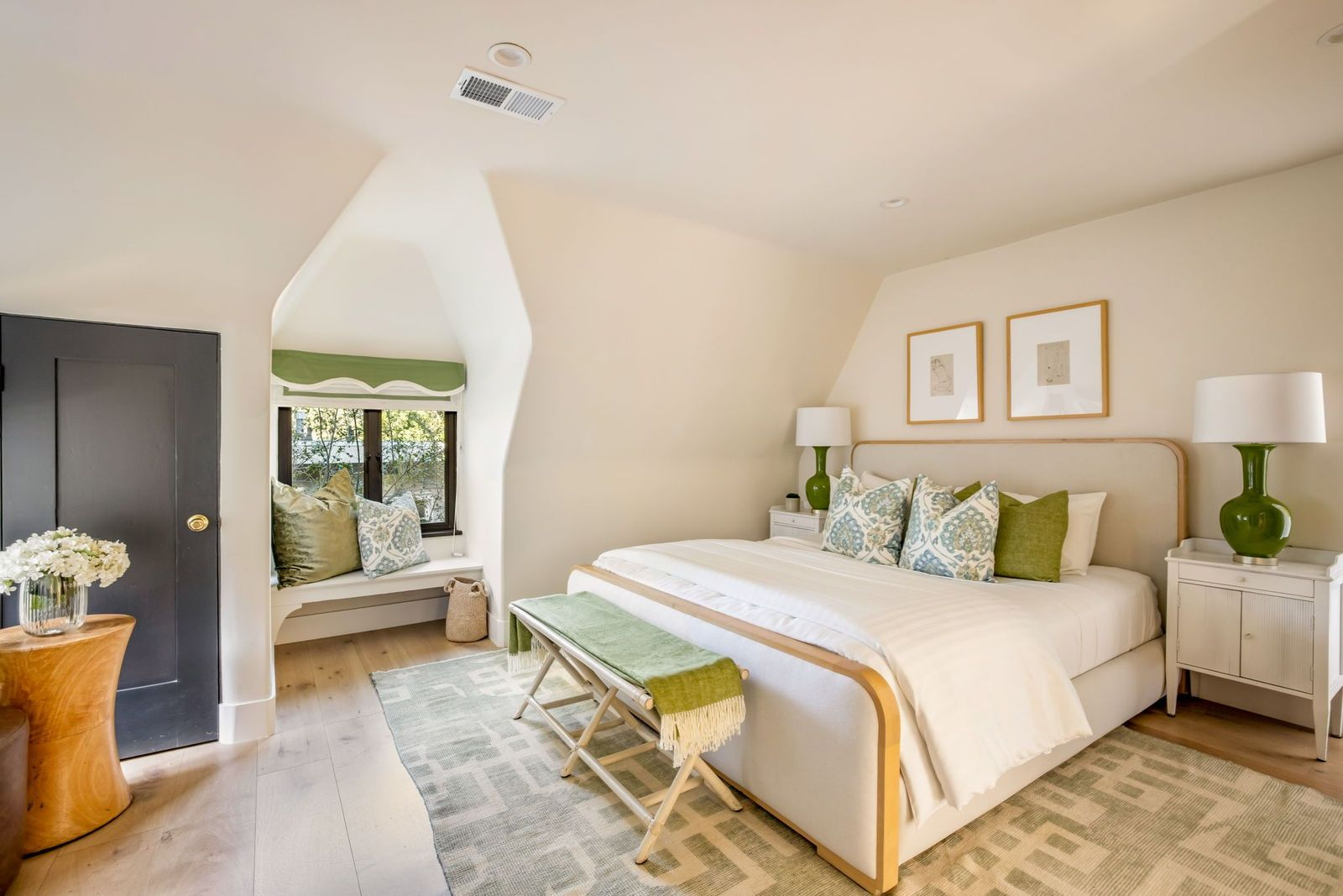 The bed sits against a cream wall, while a recessed window nook creates a built-in seating area beneath a scalloped green shade.