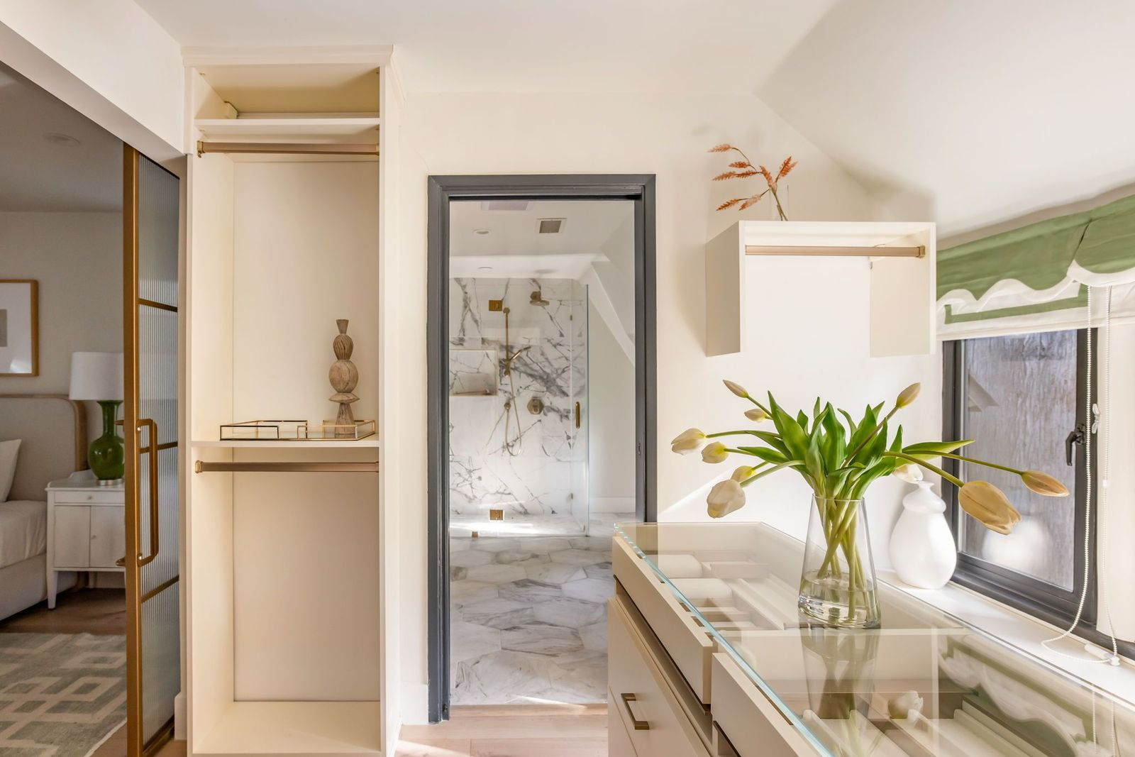 The suite's closet connects the bedroom and bathroom with custom cabinetry along the walls and a large island with a glass-topped display surface at the center.