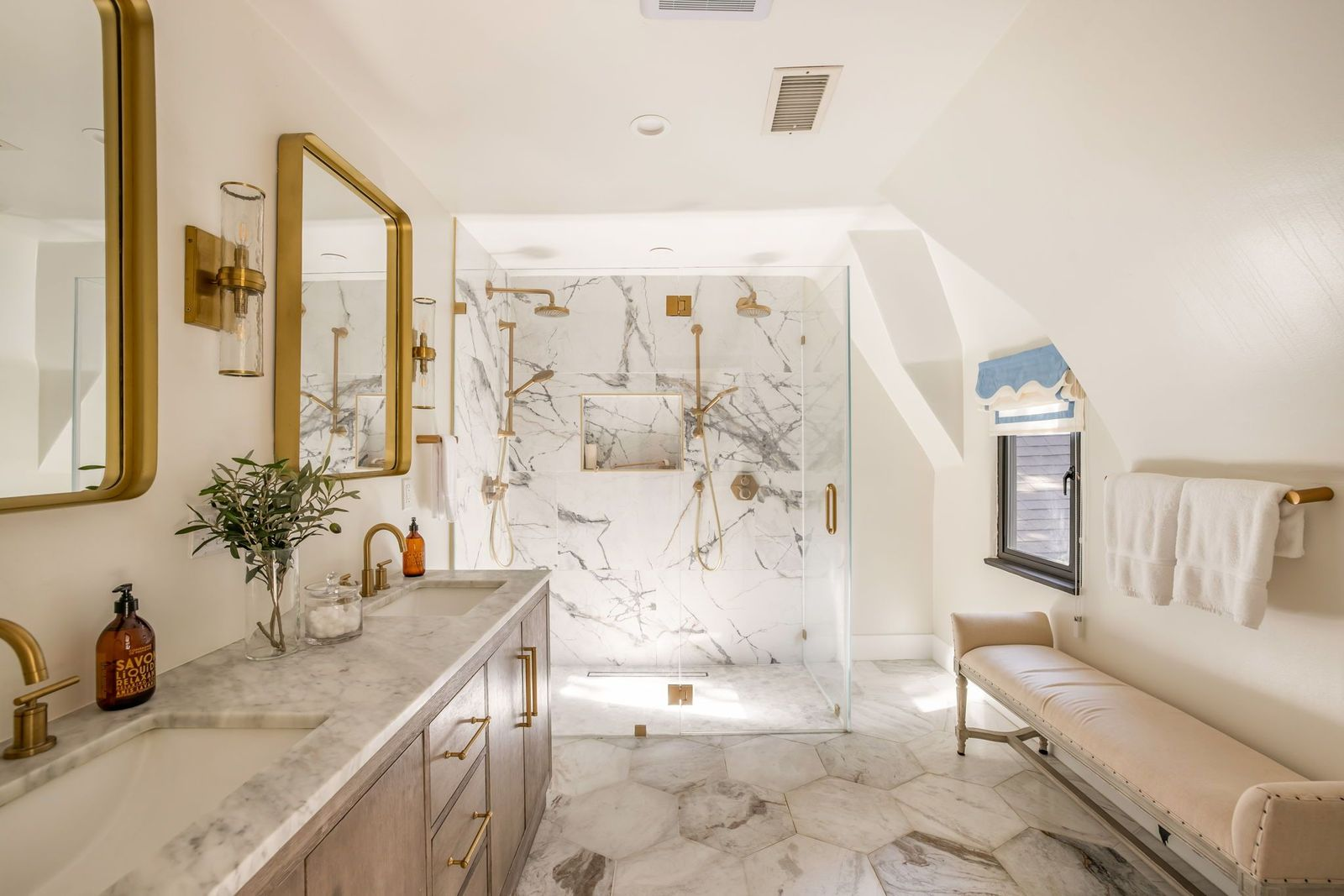 The primary bathroom is filled with marble surfaces, from the hexagon stone floor to the walls of the glass-enclosed shower.