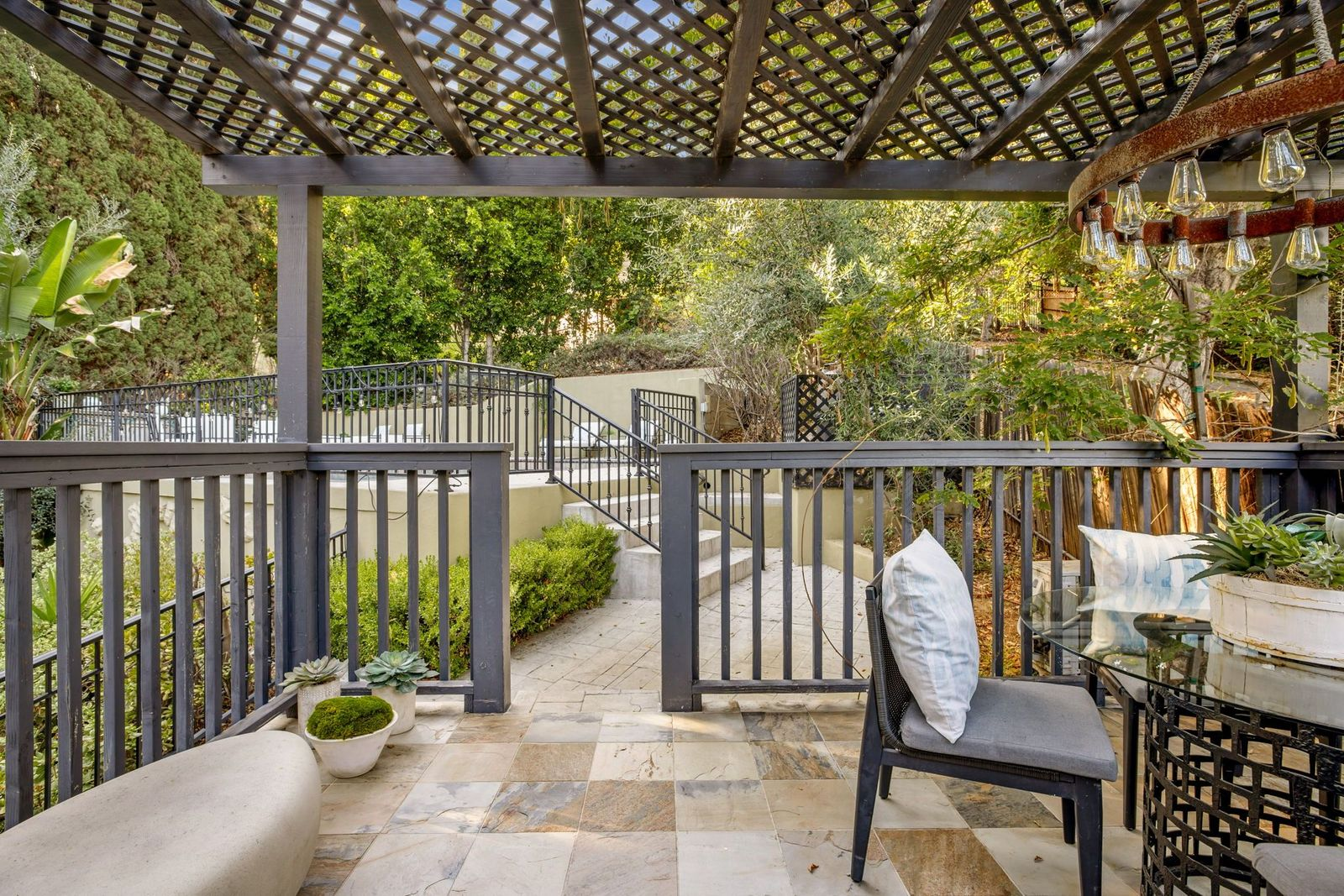 Stone tile covers the floor, while black railings frame the elevated space and a glass-topped dining table provides a spot for outdoor dining.
