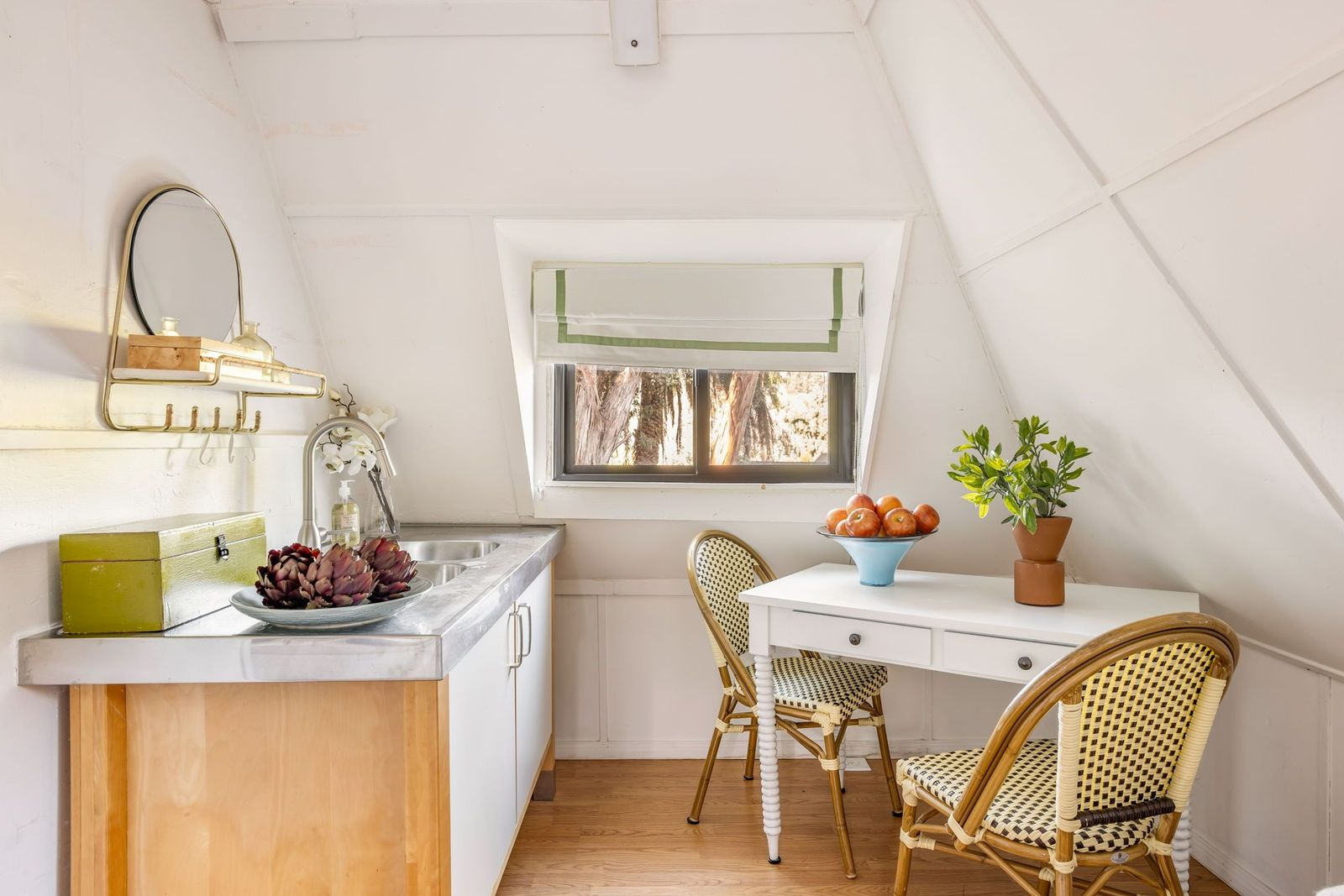 At the other end, a compact kitchenette sits beneath the sloped ceiling with a stainless-steel counter and sink, lower cabinetry, and a small dining table for two.