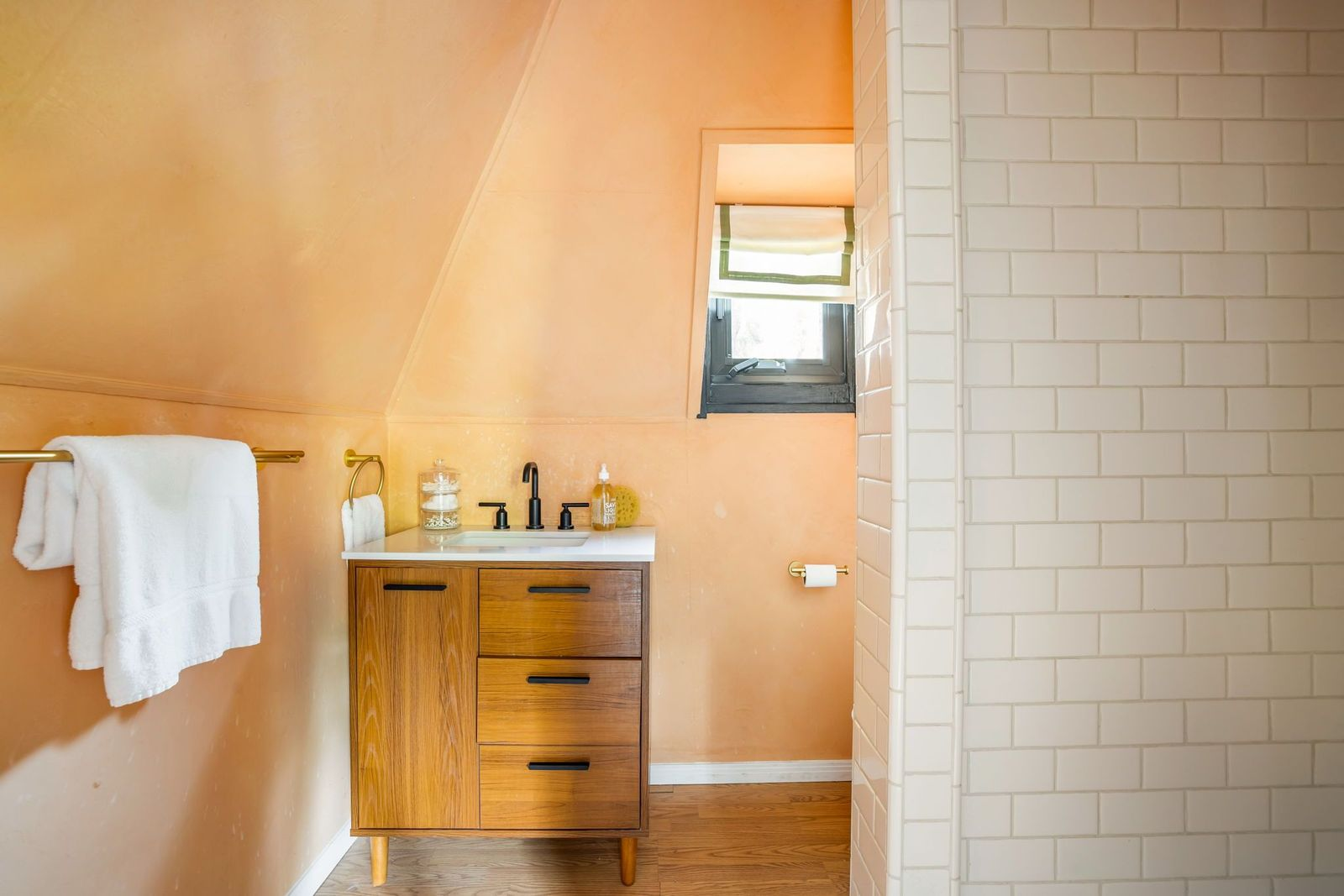 A private bathroom with warm peach-toned walls, a wood vanity, and a white tile shower.