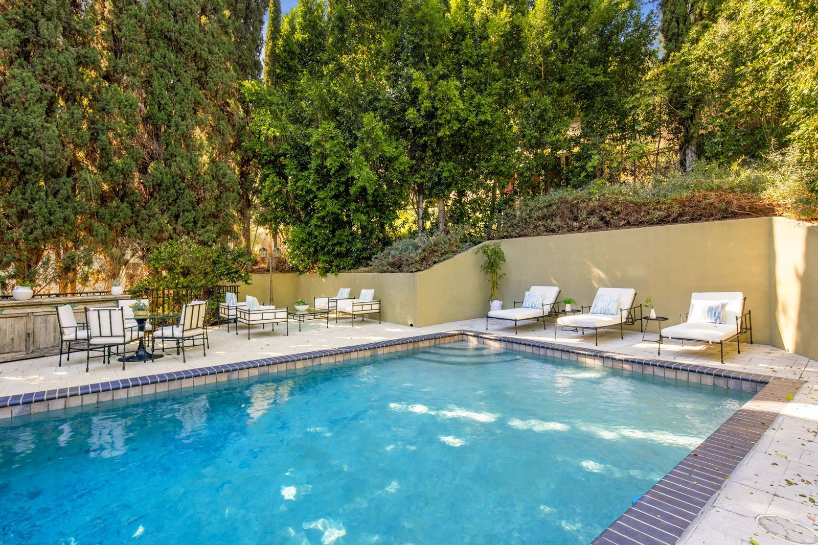 The elevated grounds open to a rectangular swimming pool surrounded by a stone patio and dense landscaping.