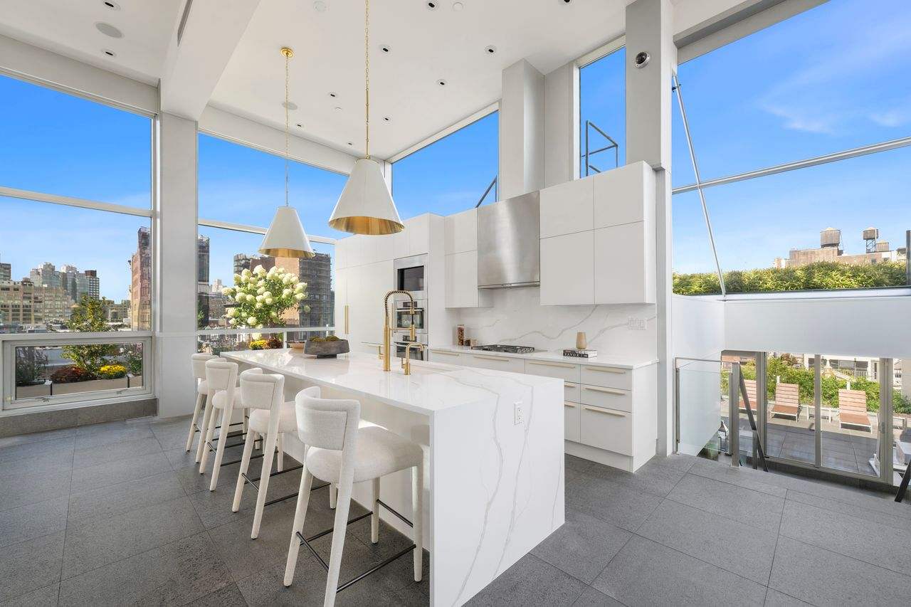 The kitchen opens around an oversized marble island that runs through the center of the space, with seating along one side and a sink on the other. 