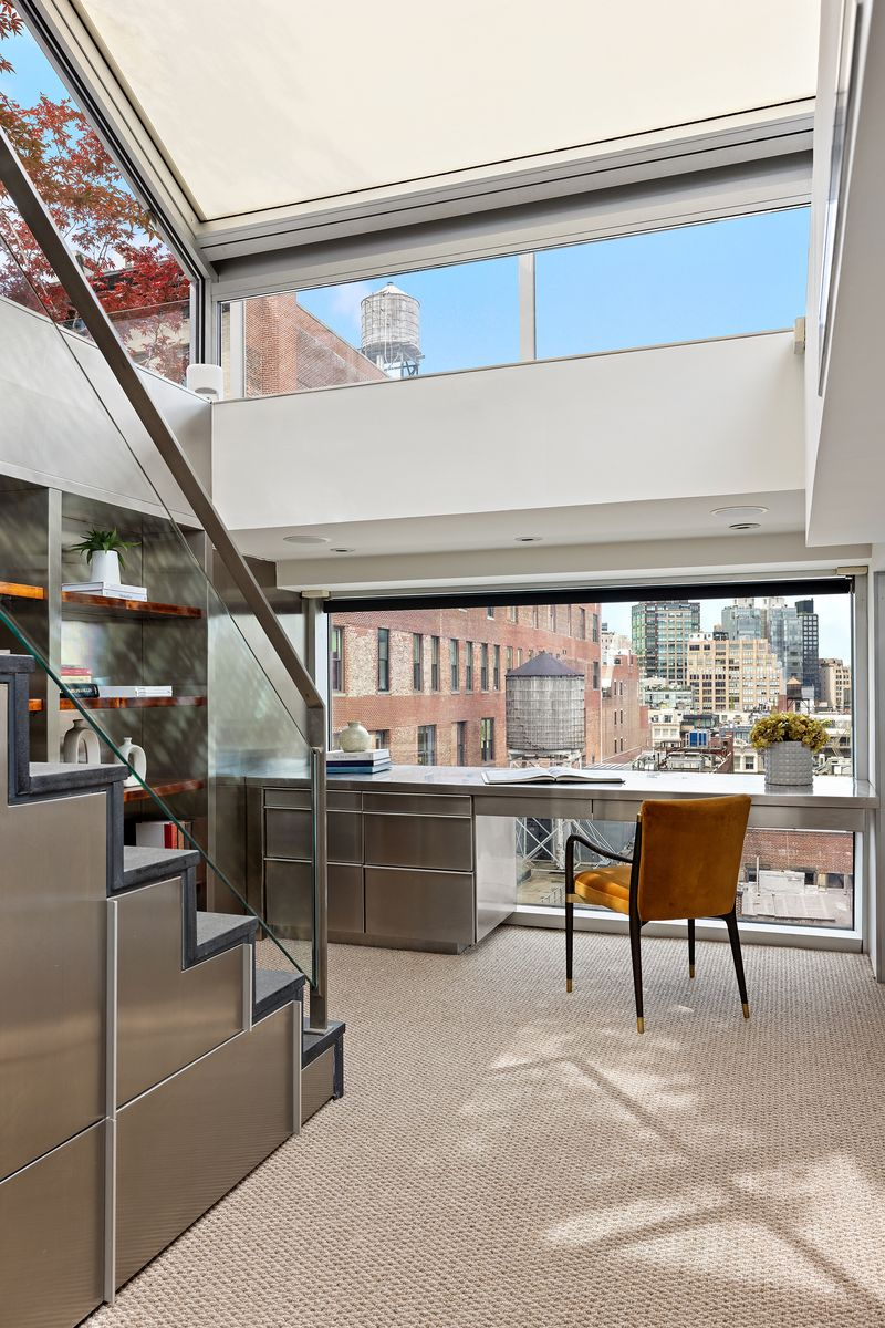 A built-in metal desk runs beneath a wide window overlooking SoHo, while open shelving lines the side wall.