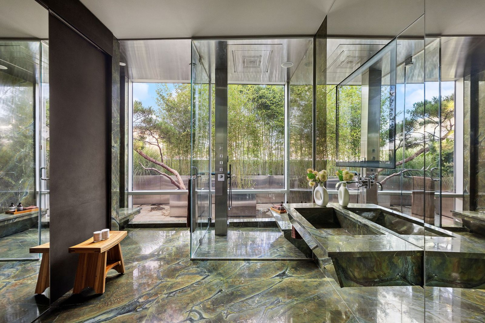 A large glass-enclosed shower sits in the far corner, while mirrored walls reflect the stonework and the trees along th private terrace.