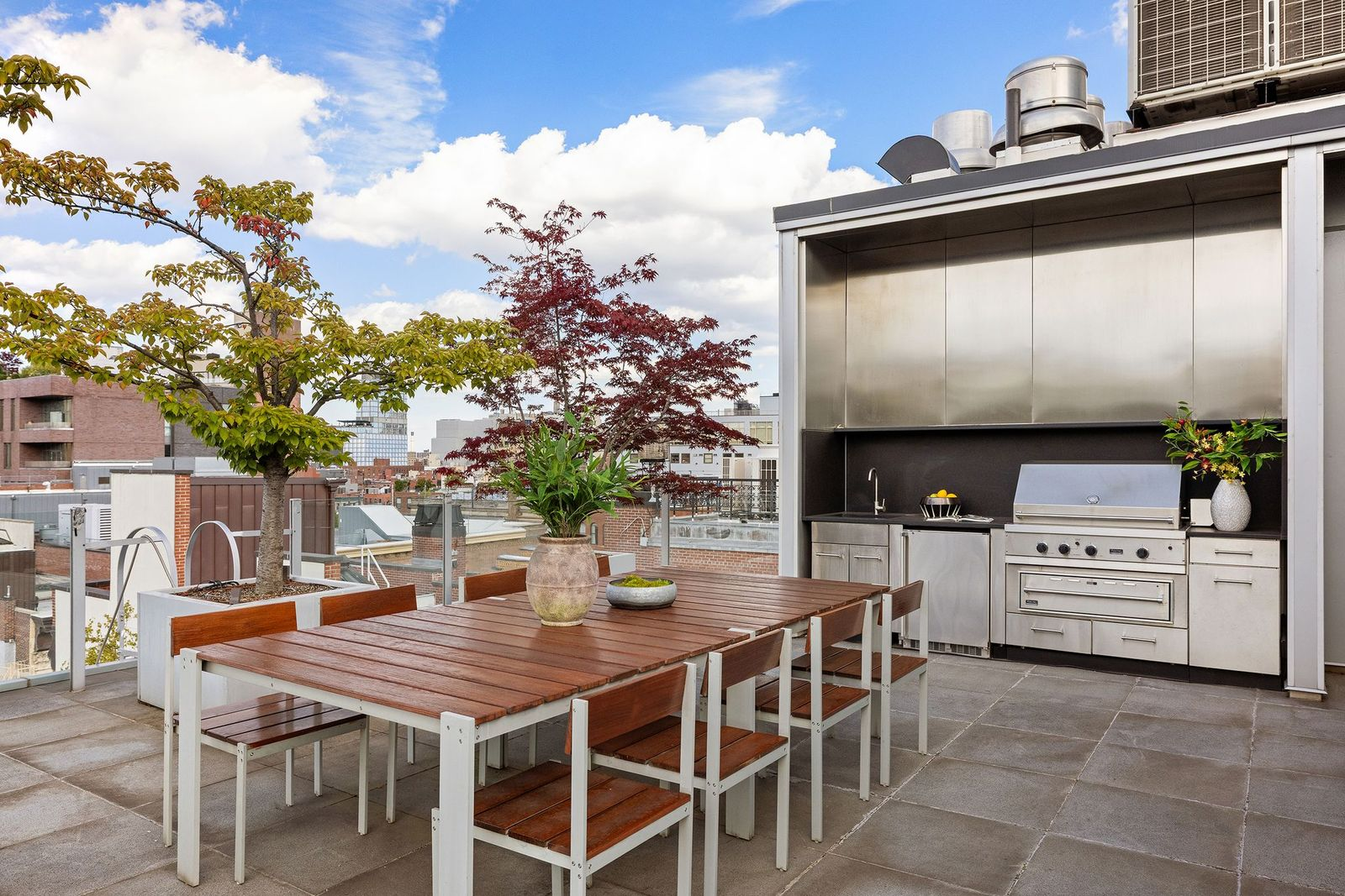 A separate dining area sits beside a built-in outdoor kitchen with a grill, sink, and storage.