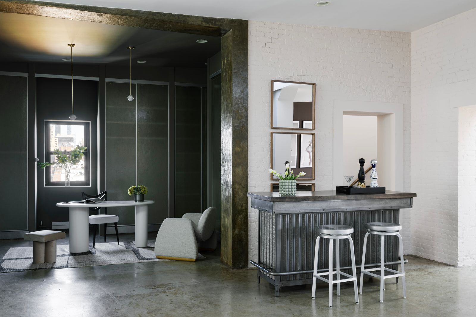 A compact bar is set against the white brick wall, with a metal counter and two stools.