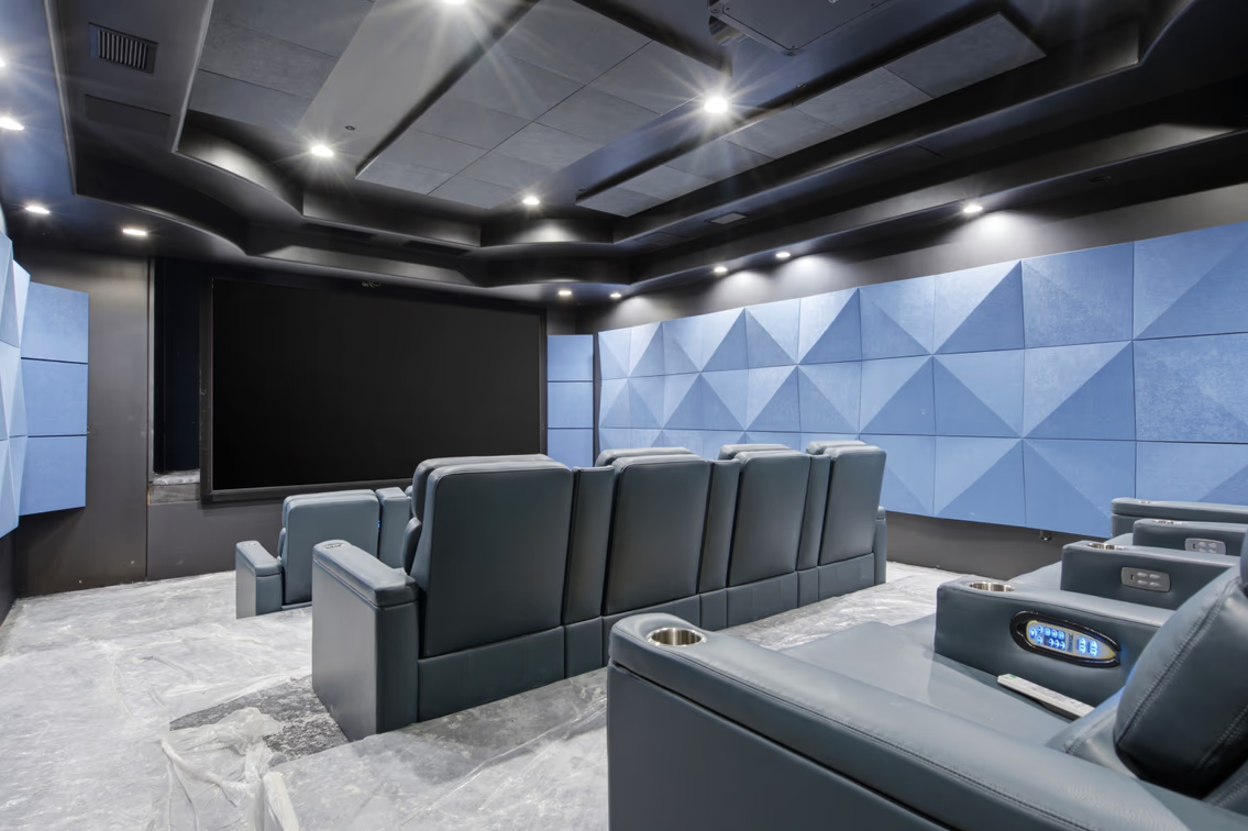 Tiered rows of oversized reclining seats face a large projection screen with blue geometric acoustic panels running along the side walls to help control sound.