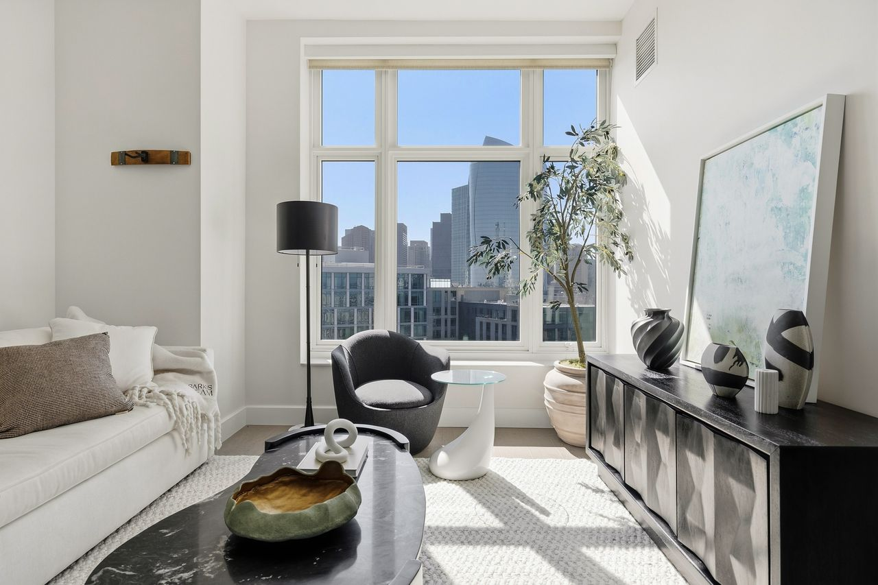The main living space opens beneath tall ceilings and a wall of oversized windows overlooking the Boston skyline. 