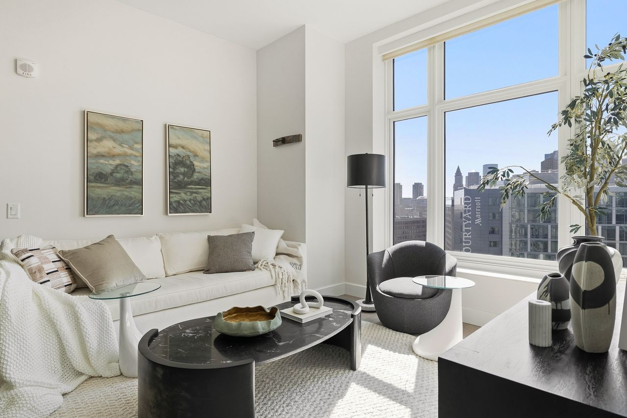 A low sofa and lounge chair sitting across from a cabinet topped with a variety of art pieces.