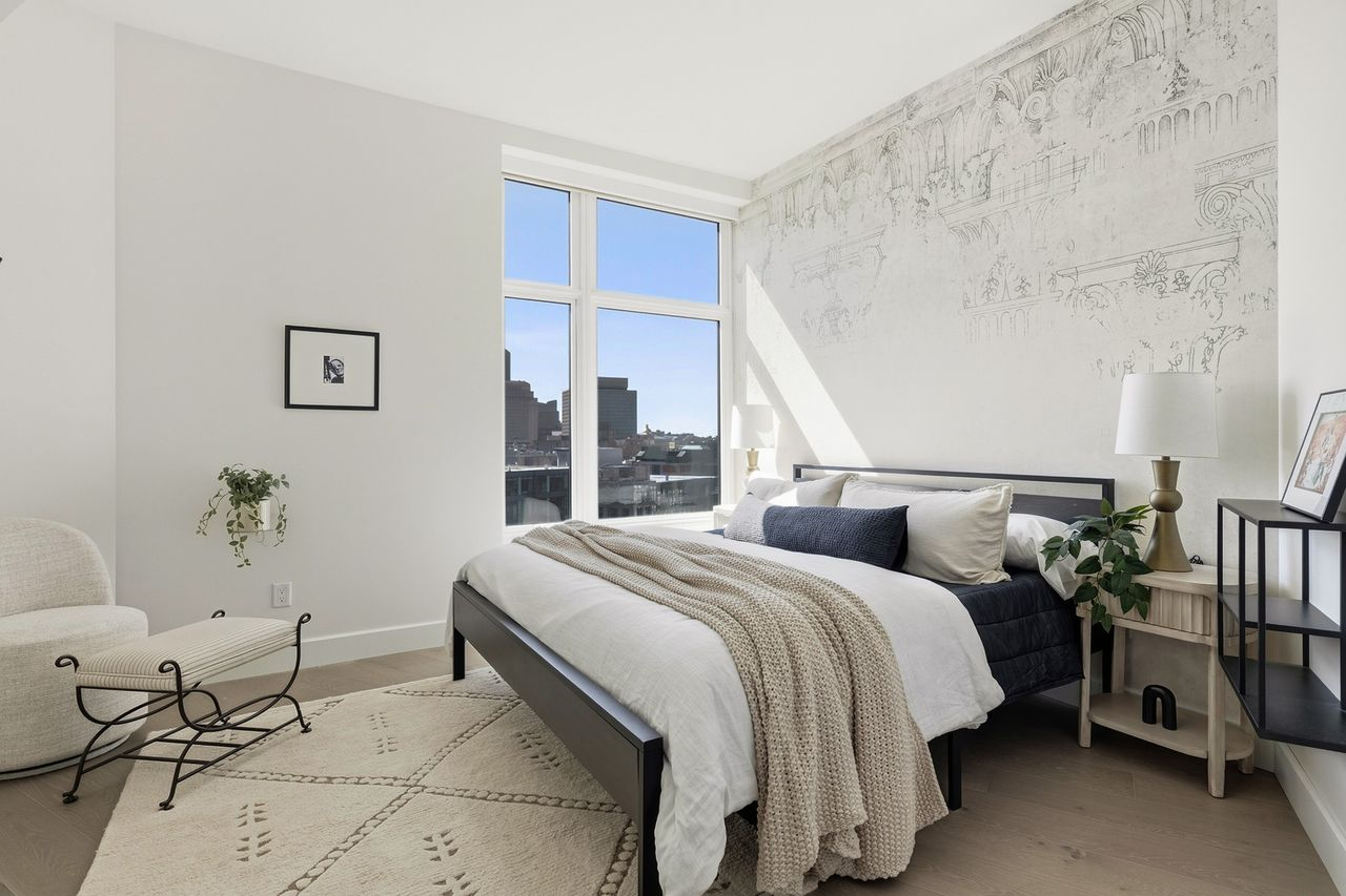 Primary suite's bedroom is framed by a tall window with the bed sitting against a wall illustrated with faint architectural linework that resembles classical buildings and columns.