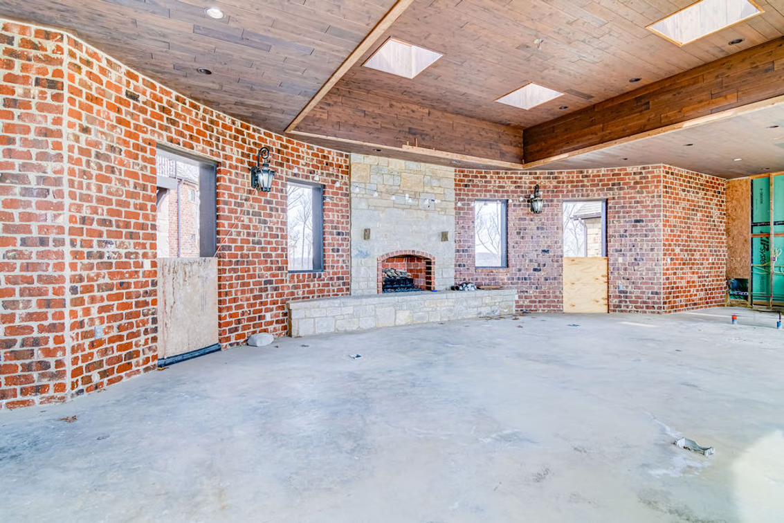 A covered outdoor lounge features exposed brick walls, a wood-plank ceiling, and a built-in stone fireplace. 