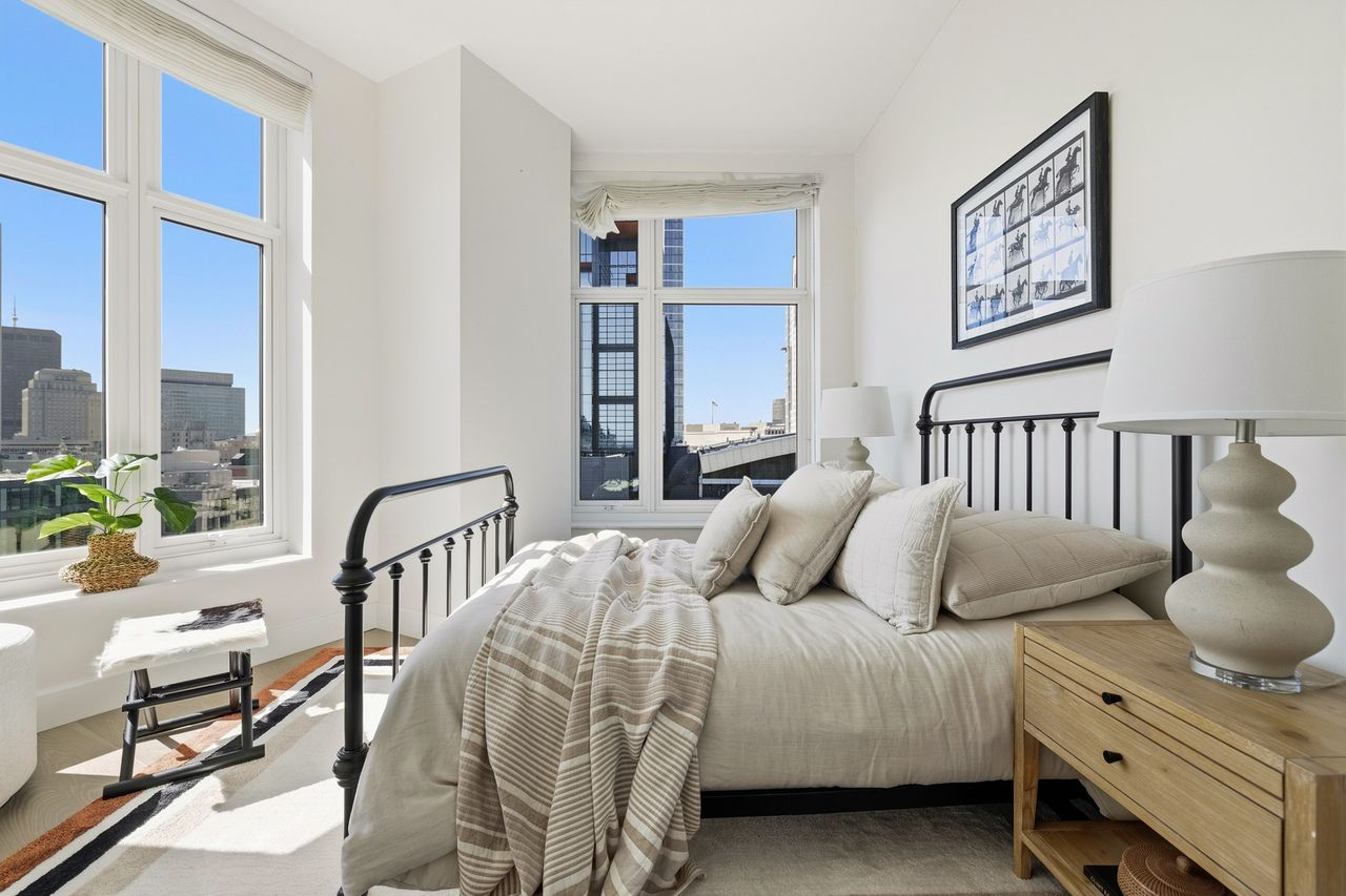 The penthouse’s second bedroom sits in a corner of the home, with tall windows lining multiple sides of the room.