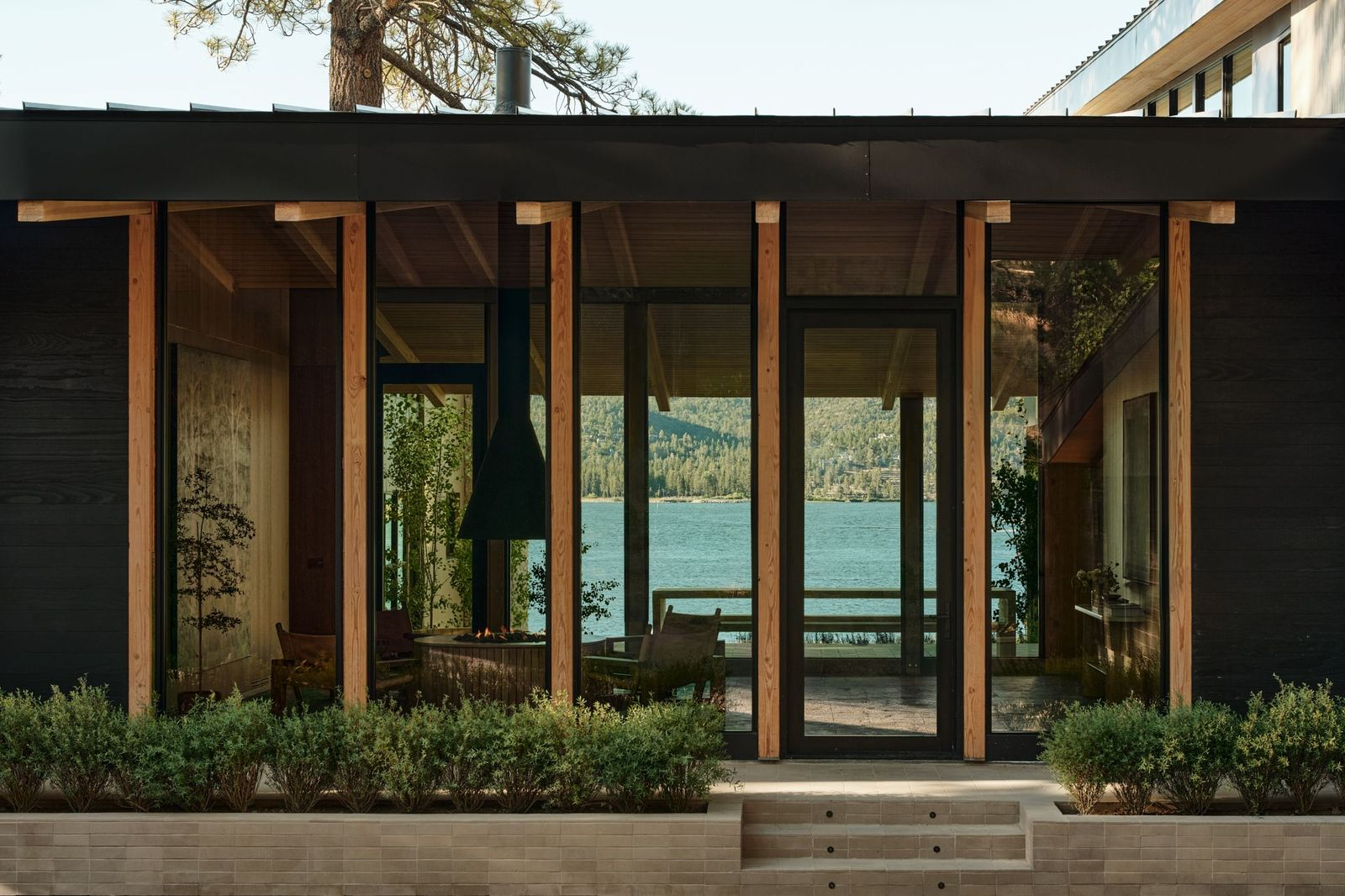 Floor-to-ceiling glass is set between exposed beams on both sides of the atrium, creating a straight-through view toward the lake.