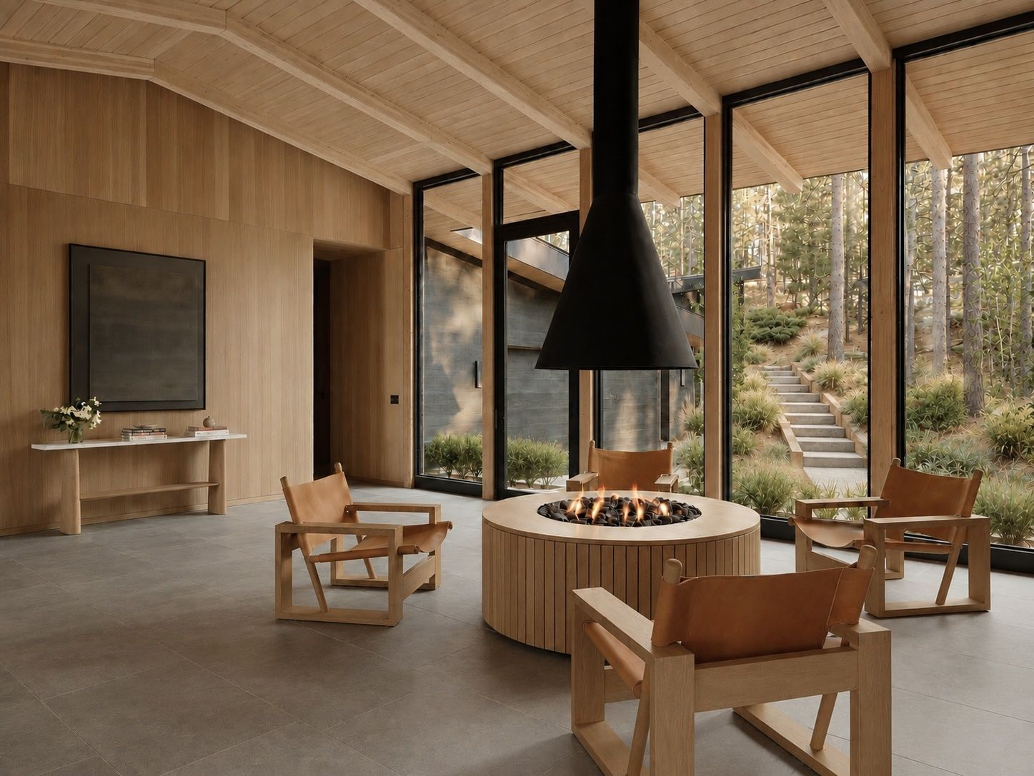 Centered between the glass walls, four chairs surround a round indoor firepit beneath a suspended black hood.