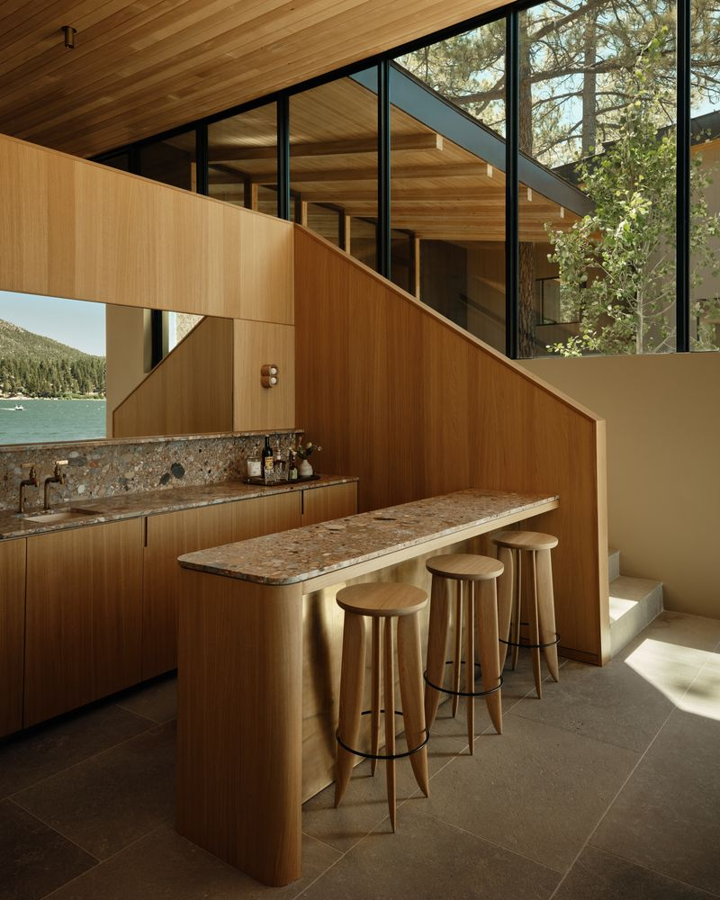 The bar sits next to a staircase with a long stone counter, lower cabinetry, and a raised ledge lined with stools.