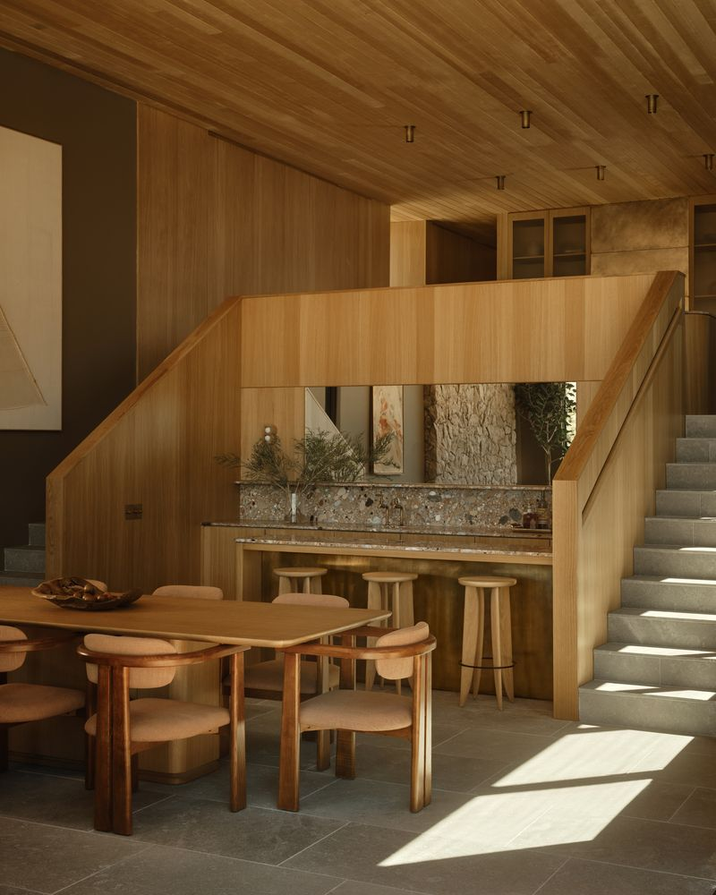 From the kitchen, a dual staircase drops down to the dining area, with the two sides opening around a built-in bar positioned directly between them. 