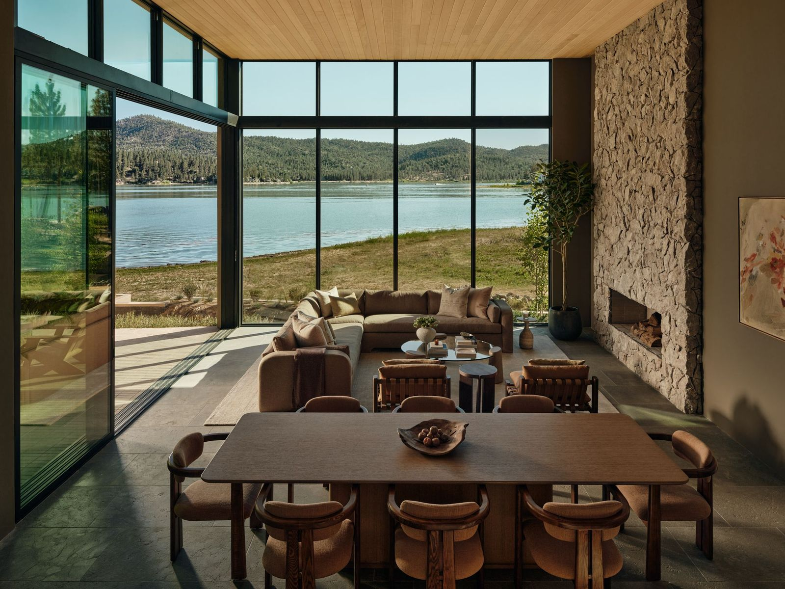 The living room sits directly against the corner glass walls, with the couch facing a dry-stacked stone fireplaces.