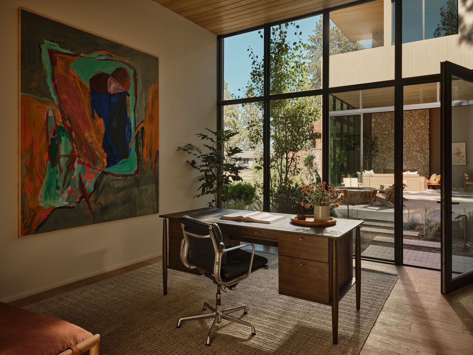 The office places a dark wood desk and chair directly across from the glass wall overlooking the courtyard.