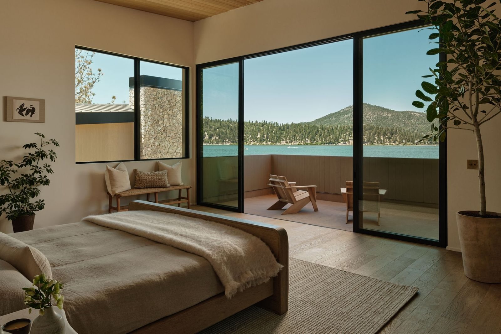 The first suite places the bed directly across from a glass wall that opens to a patio with a lakefront view.