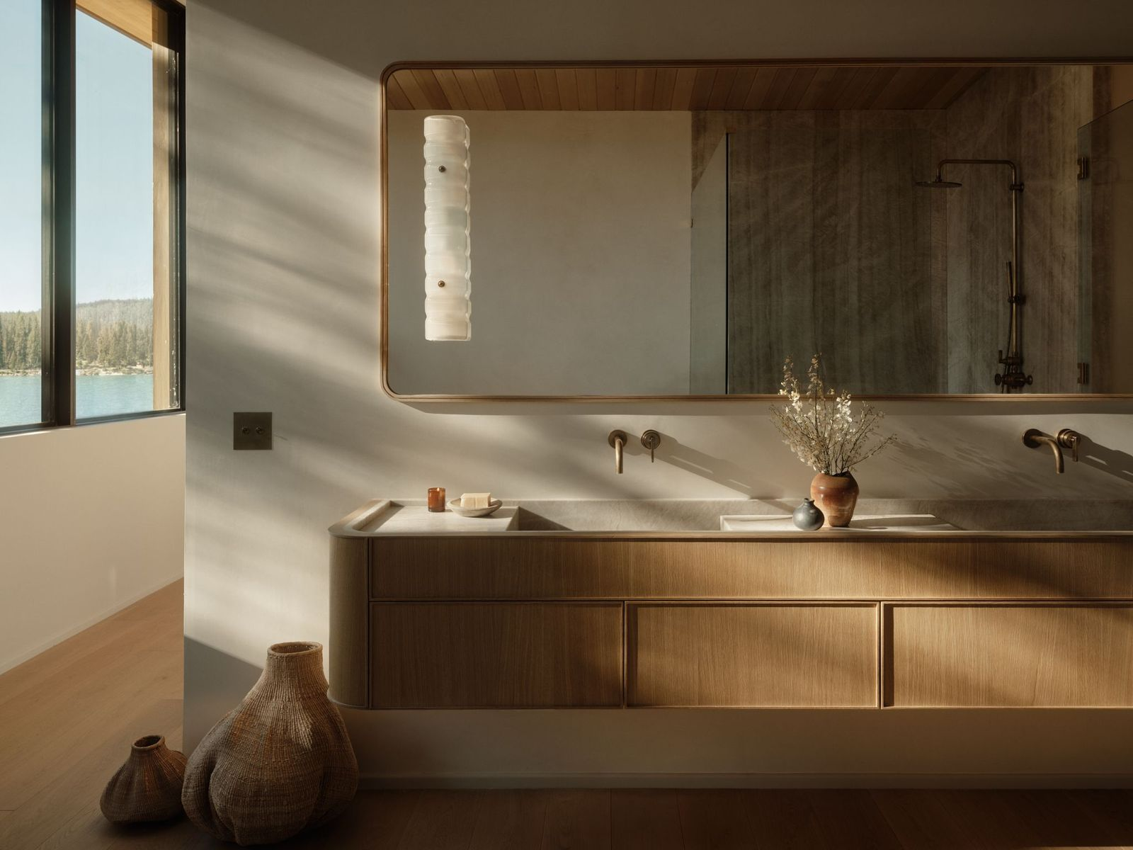 A stone soaking tub runs beside a glass-enclosed shower, with the same grey stone extending across the shower walls, bench, and tub.