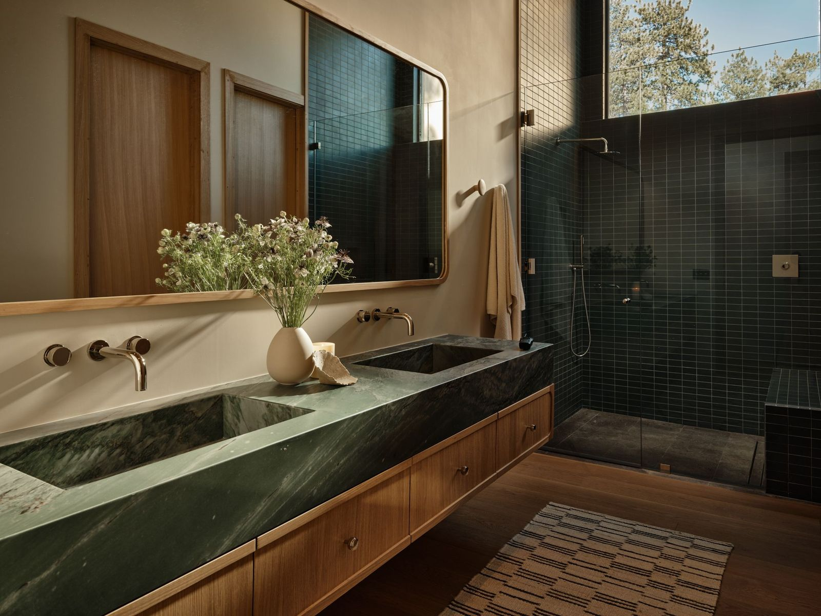 Bathroom with a green stone double vanity set between white oak cabinetry and a large mirror stretching the full width of the counter. 