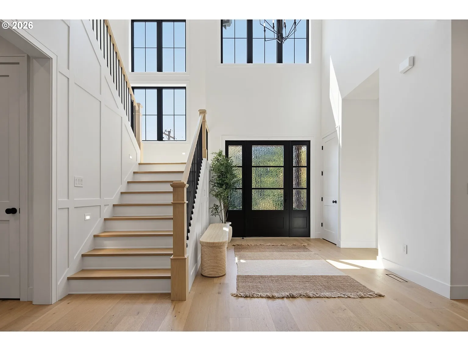 A bright double-height foyer framed by tall black-trimmed windows and a staircase rising along one side.