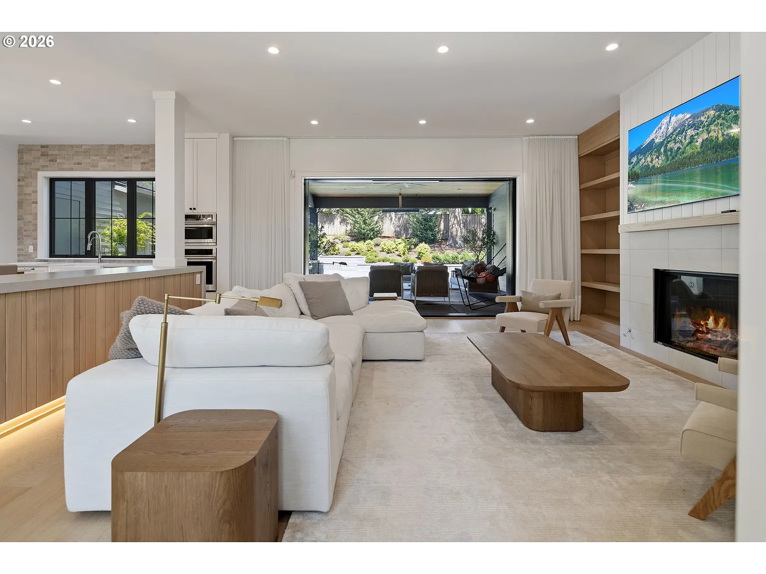 The family room has a large couch facing a fireplace and mounted TV, with light wood shelving extending along both sides.