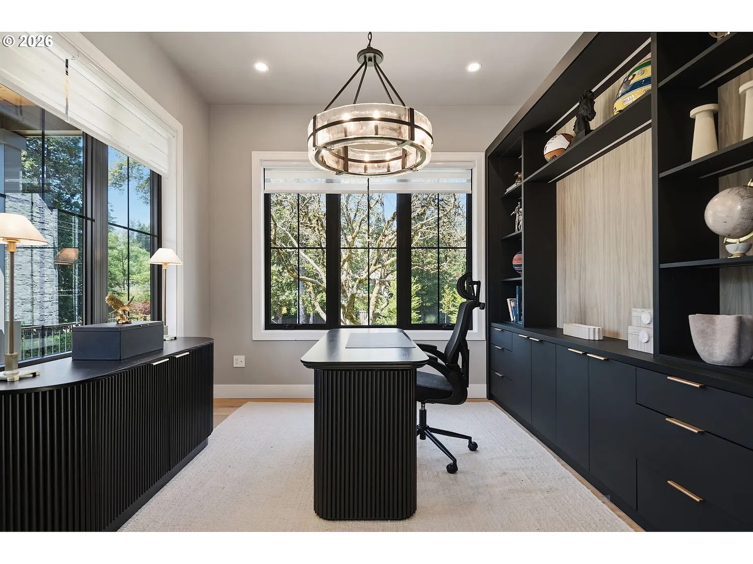 Dark built-in cabinetry fills the wall behind a desk and office chair that faces a window looking out to the front of the house.