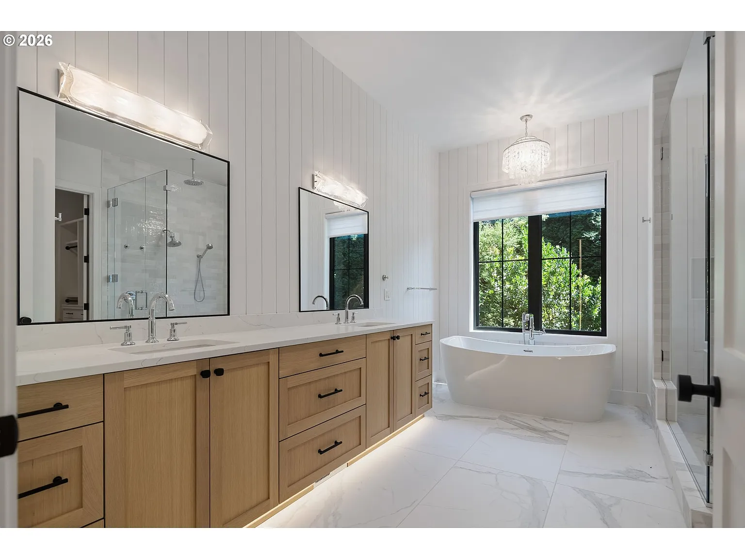 A long dual vanity stretches across one side beneath oversized mirrors, while a freestanding soaking tub is centered beneath a black-framed window.