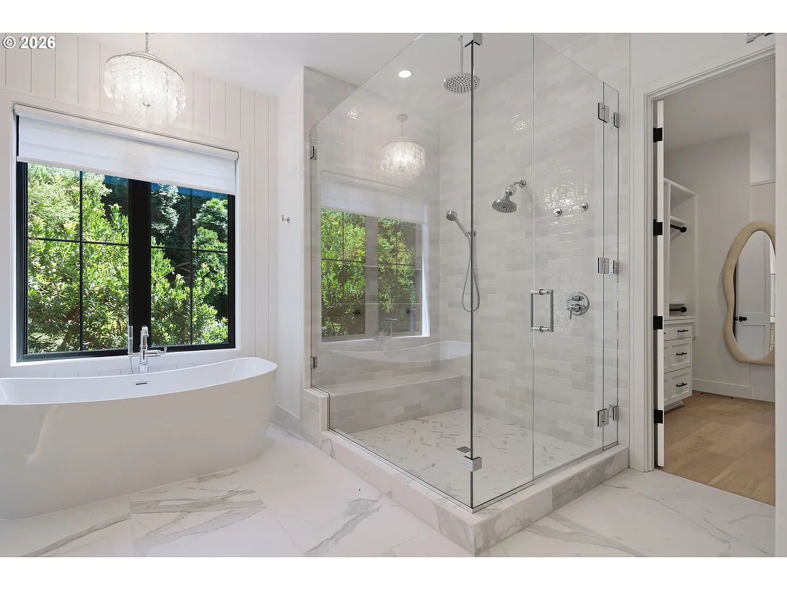 On the other side of the tub, a large glass-enclosed shower has multiple shower fixtures, including an overhead rain head and handheld system.