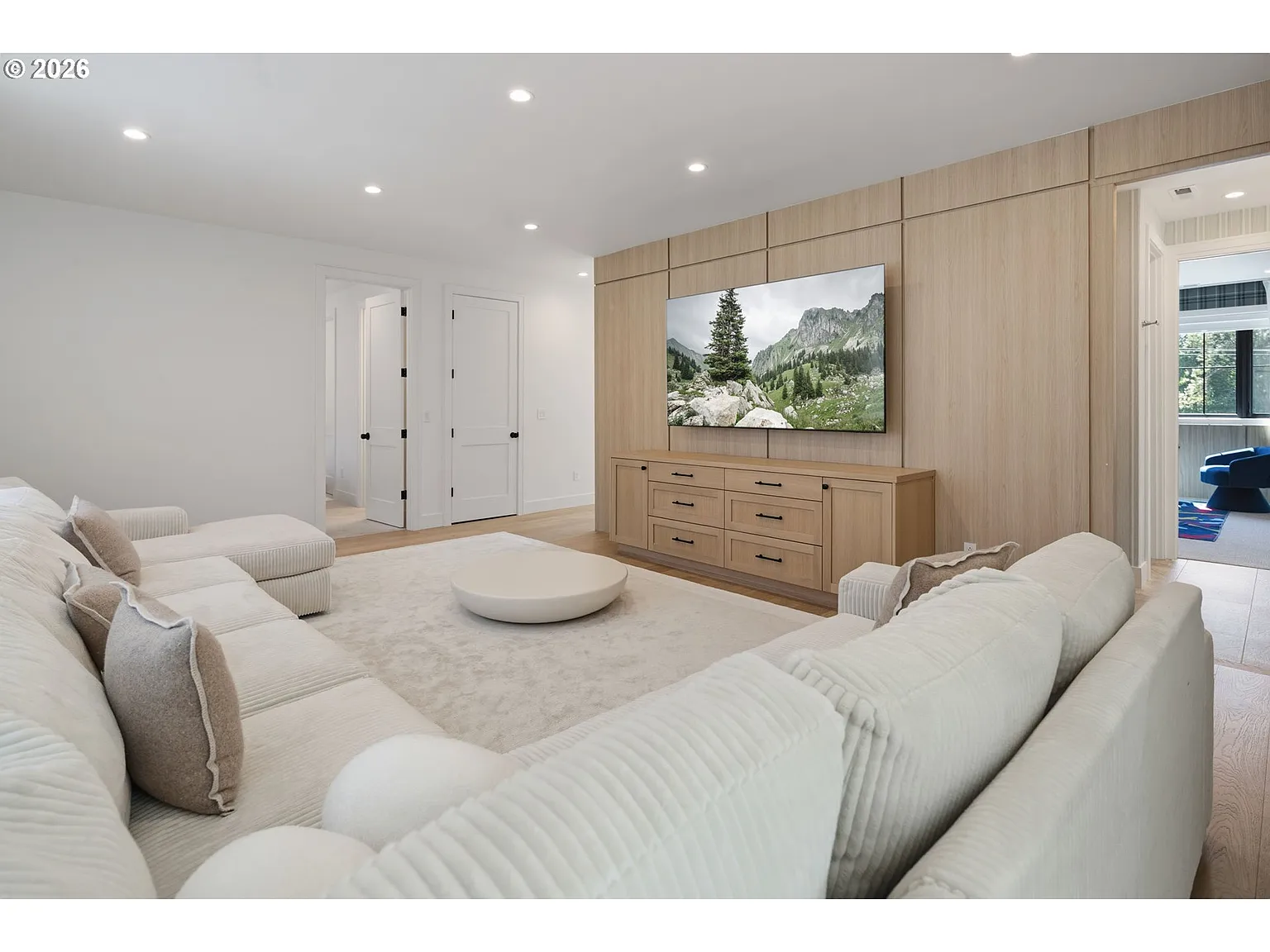 A central media lounge, with an oversized couch facing a TV set into a full light wood feature wall.
