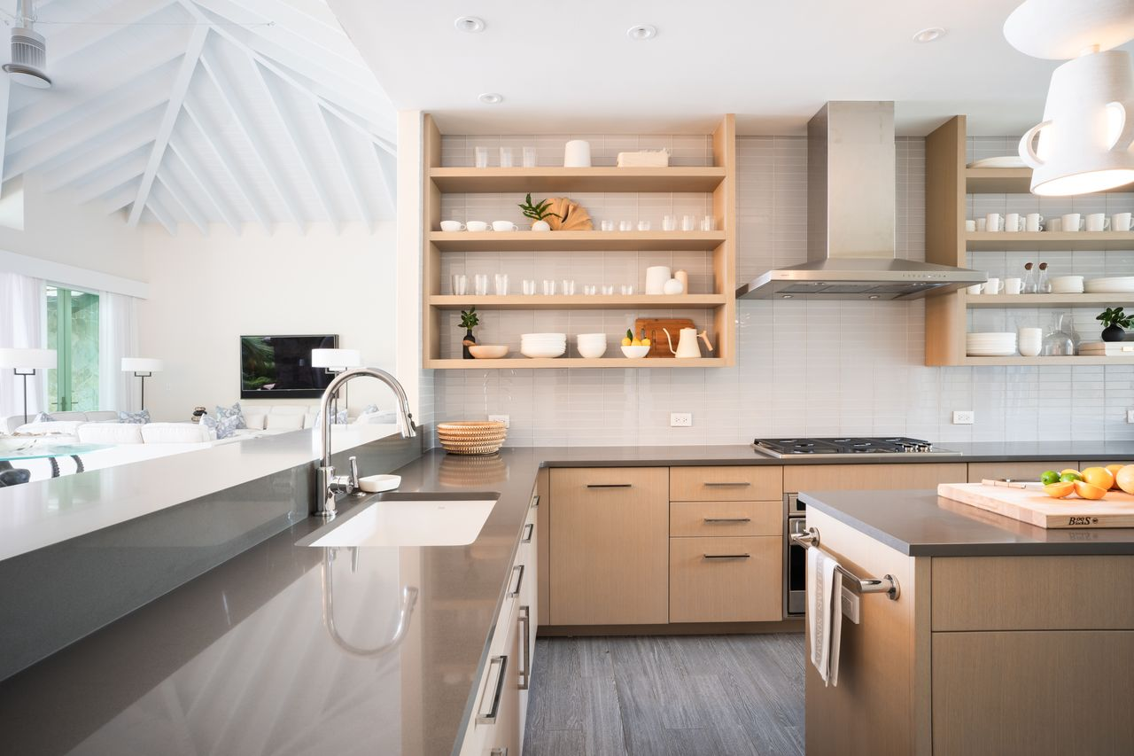 The kitchen opens to light wood cabinetry, long stretches of gray countertops, and open shelving running along the backsplash. 