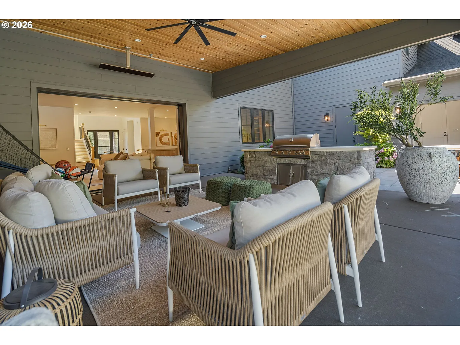 A full outdoor seating arrangement is gathered around a low central table, creating a shaded lounge with a built-in barbecue station just outside the living room.