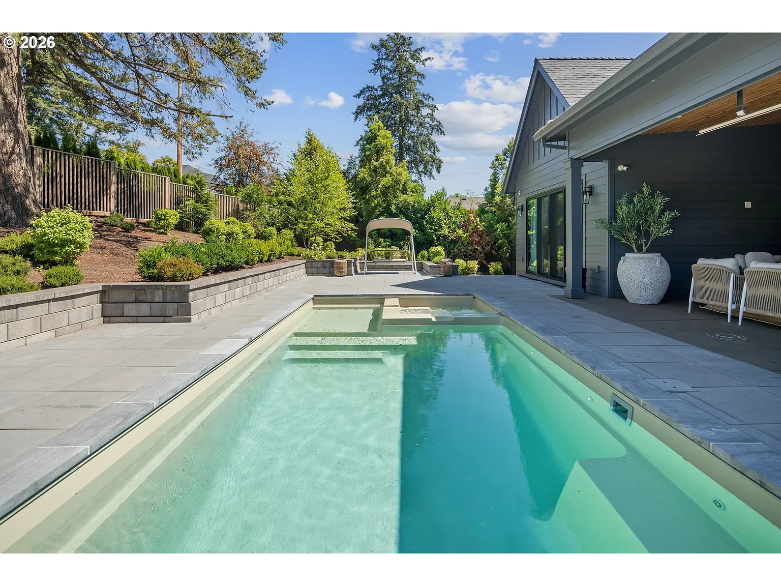 Past the covered lounge, the patio opens to a rectangular pool surrounded by paved terraces for sunning and casual seating. 