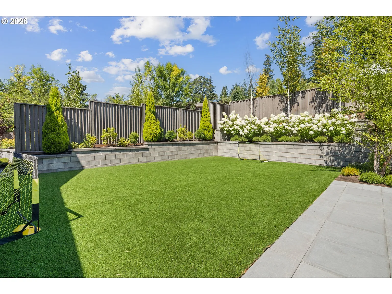 In the far corner of the yard, the hardscaping gives way to a large turf lawn bordered by raised planting beds. 
