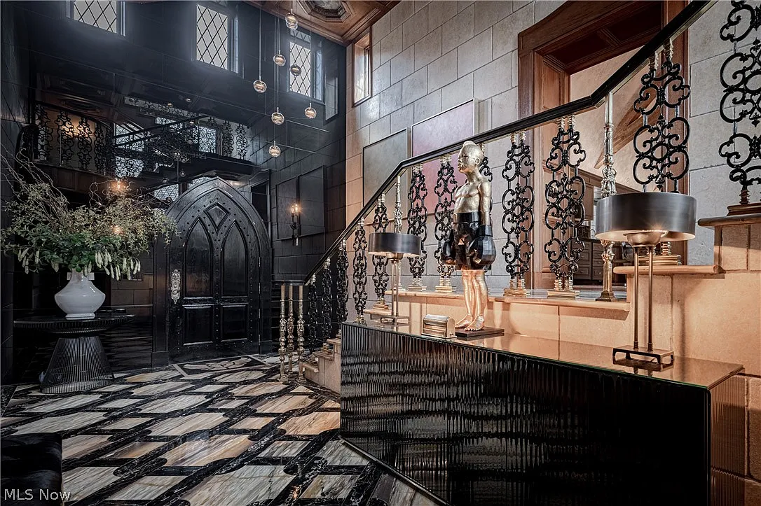 Tall leaded-glass windows rise beside the staircase and above the front door, pulling natural light into the double-height space and highlighting the mix of stone, wood, and metal.