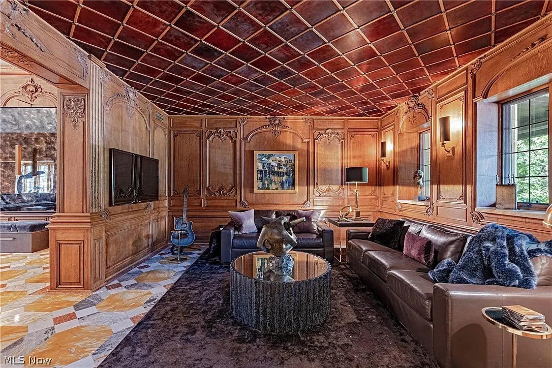 The grand salon walls are wrapped in hand-carved wood paneling, with decorative moldings and inset details framing the room beneath a coffered ceiling.